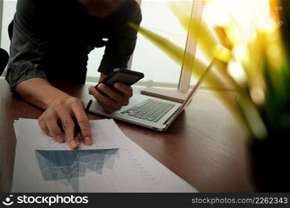 businessman hand working with new modern computer and smart phone with business strategy documents with green plant foreground on wooden desk in office
