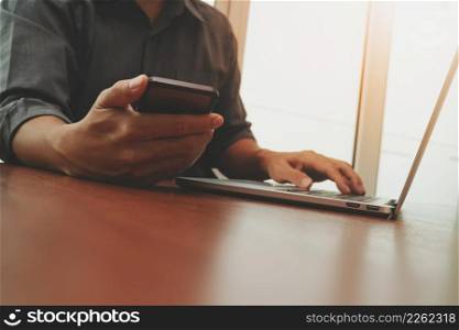 businessman hand working with smart phone and new modern computer on wooden desk in office