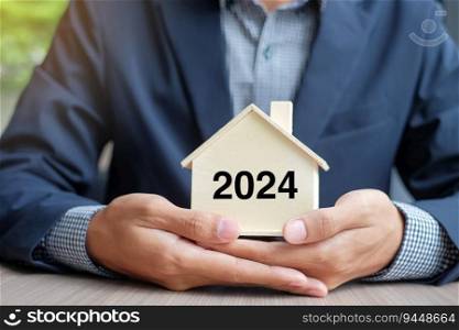 Businessman hands holding wooden House model with 2024 New Year text. Property insurance and real estate concepts