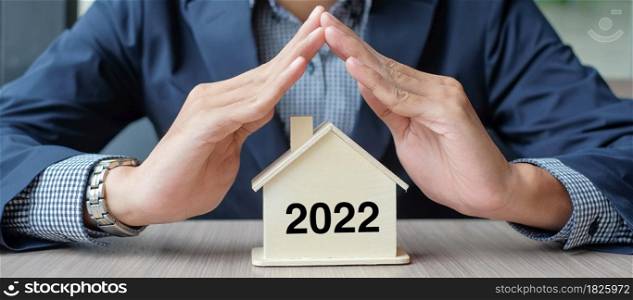 Businessman hands over wooden House model with 2022 New Year text. Property insurance and real estate concepts