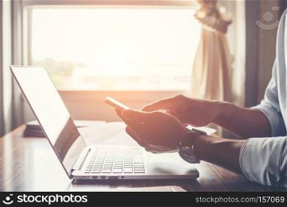 Businessman hands using cell phone with laptop at office desk.