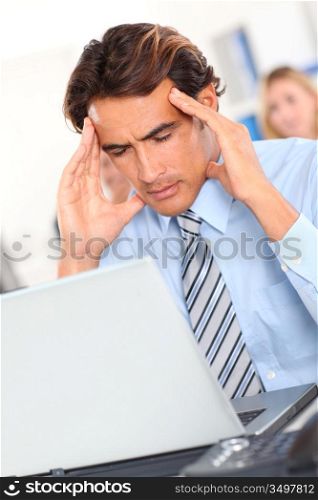 Businessman having a headache in front of laptop