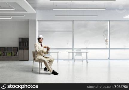 Businessman having coffee break. Elegant businessman in white suit sitting on chair in office interior