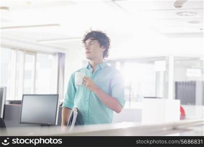 Businessman having coffee while holding files in creative office