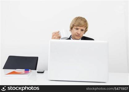 Businessman having coffee while using laptop in office