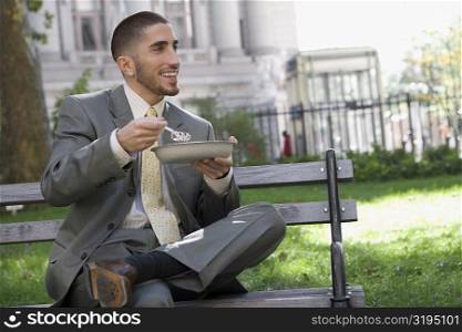 Businessman having food on a park bench