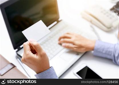 businessman hold blank paper card on hand with office desk background