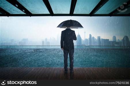 Businessman hold umbrella stand on rooftop ,raining day with city skyline view , risk and crisis concept .