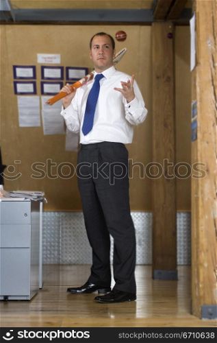 Businessman holding a cricket bat and tossing a cricket ball in the air