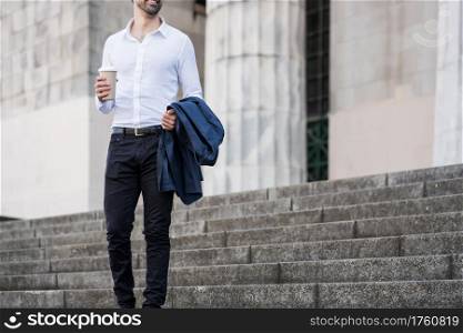 Businessman holding a cup of coffee on his way to work outdoors. Business concept.