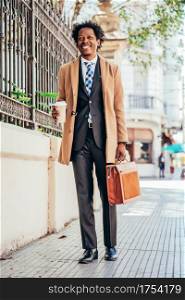Businessman holding a cup of coffee while walking on his way to work outdoors on the street. Business concept.