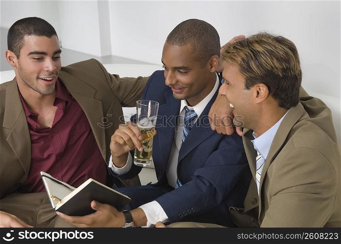 Businessman holding a glass of beer with two businessmen sitting beside him