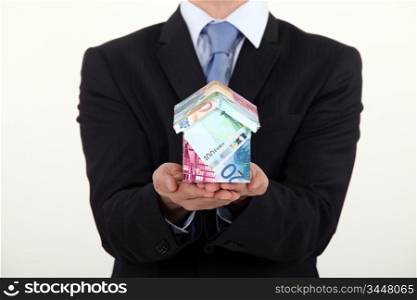 Businessman holding a house made of money