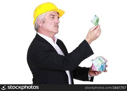 businessman holding a little house made of bills