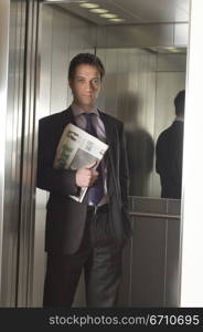 Businessman holding a newspaper in an elevator