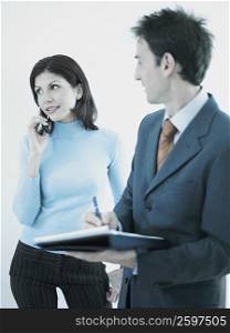 Businessman holding a personal organizer and looking at a businesswoman using a mobile phone