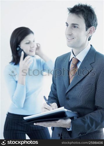 Businessman holding a personal organizer with a businesswoman talking on a mobile phone behind him