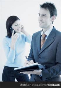Businessman holding a personal organizer with a businesswoman talking on a mobile phone behind him