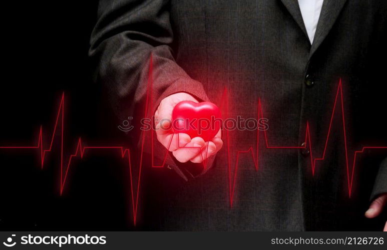 businessman holding a red heart on a black background, in front of him is a cardiogram. Office workers cardiovascular disease concept