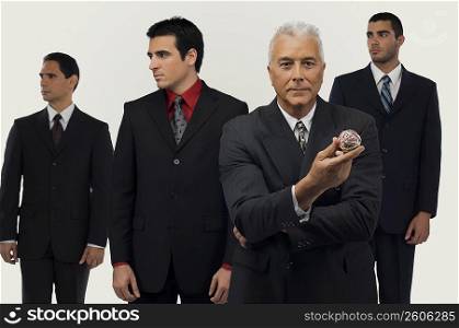 Businessman holding a rubber band ball with three businessmen standing behind him and looking away