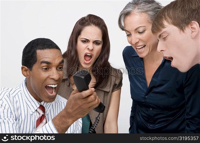 Businessman holding a telephone with three business executives shouting