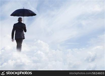 Businessman holding an umbrella and walking away in dreamlike clouds
