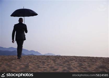 Businessman holding an umbrella and walking away in the middle of the desert