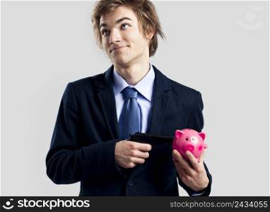 Businessman holding and pointing a gun to a piggy bank
