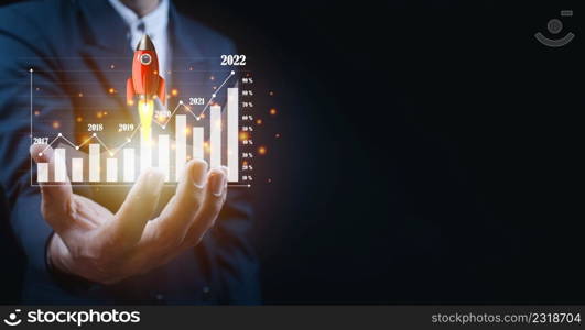 Businessman holding and showing a growing virtual hologram of statistics, graph and chart with arrow up on dark background. Stock market. Business growth, planing and strategy concept