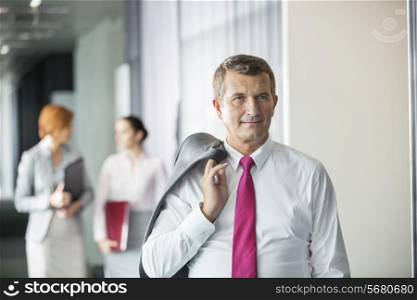 Businessman holding coat over shoulder with female colleagues in background at office