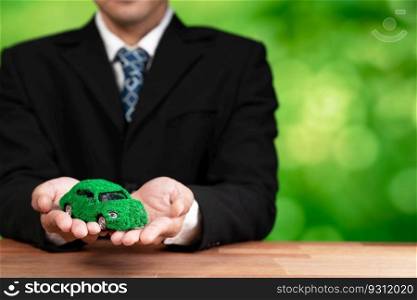 Businessman holding green eco car model in office. Electric vehicle utilized by eco-friendly business for environmental friendly transportation. Corporate responsible with zero CO2 emission. Alter. Businessman holding green eco car model in office. Alter