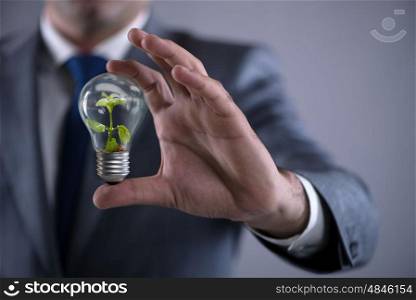 Businessman holding lamp in green environment concept