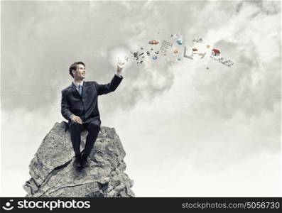 Businessman holding mobile phone. Young businessman sitting on top of rock with mobile phone in hand