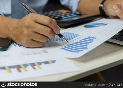 businessman holding pen to work computer graphs and charts data statistical data financial analysis documents.