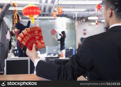 Businessman holding red envelopes and coworkers hanging decorations for Chinese new year