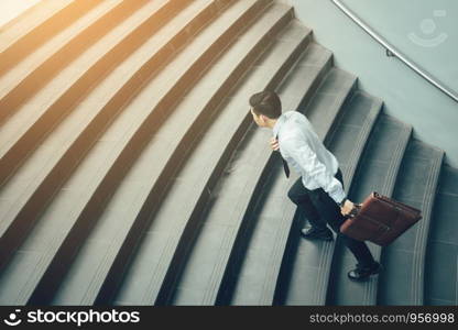 Businessman holding suitcase and running on stairs.