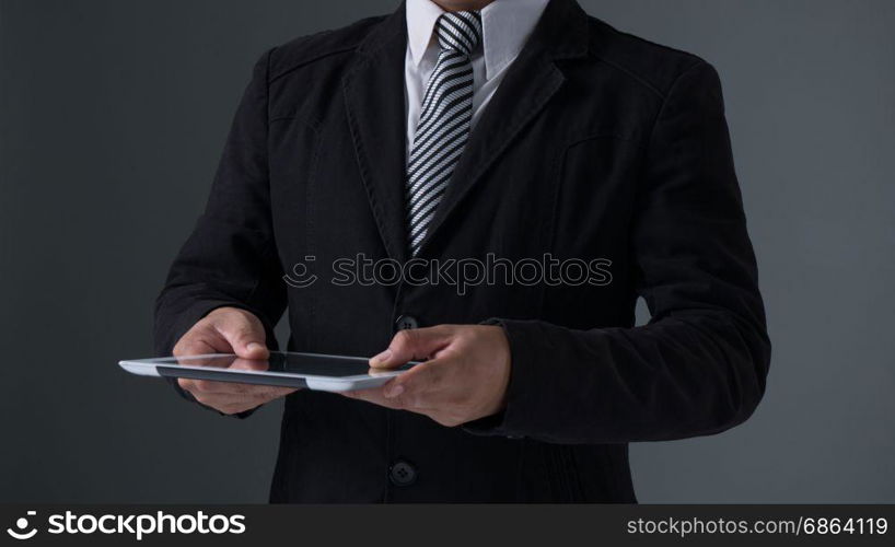 Businessman holding tablet . Businessman holding tablet in black suit on gray background