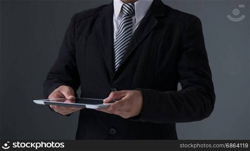 Businessman holding tablet . Businessman holding tablet in black suit on gray background
