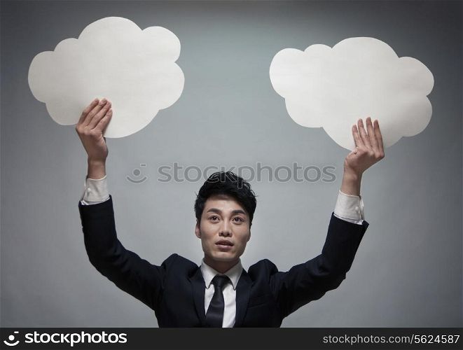 Businessman holding two paper clouds, studio shot