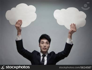 Businessman holding two paper clouds, studio shot
