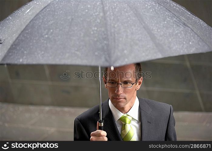 Businessman holding umbrella in front of building elevated view