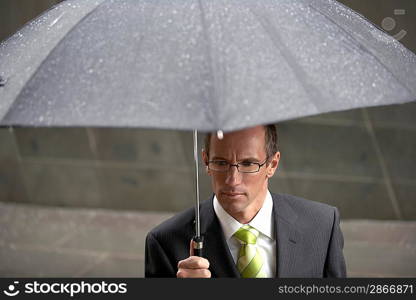 Businessman holding umbrella in front of building elevated view