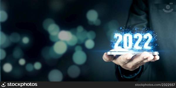 Businessman holding virtual 2022 number with blue bokeh background and copy space for merry Christmas and happy new year concept.