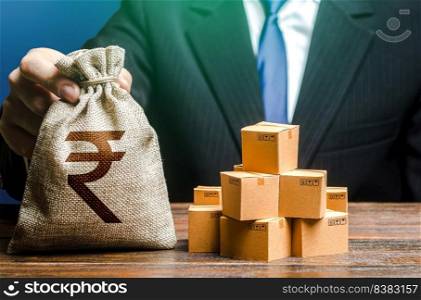 Businessman holds indian rupee money bag and boxes with goods. Import and export. Business income. Payment of taxes and fees. Advertising budget. Purchase and sale of goods, trade and commerce.