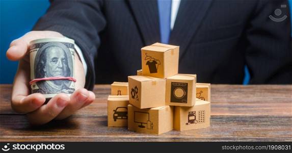 Businessman holds out a bundle of dollars near a pile of boxes. Profit, Superprofits. Investments financing in production, taxes, income revenues. Trade and exchange goods, offers for cooperation.