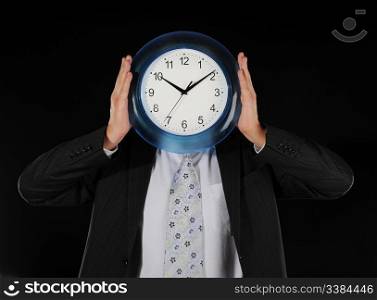 businessman in a black shirt holds clock in the face of on a black background