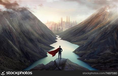 Businessman in a suit and cape hero on top of the hill watching wonderful scenery in mountains with lake during dramatic sunrise .Business ambition and success concept.