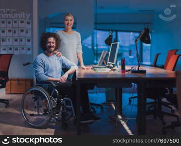 Businessman in a wheelchair in modern coworking office space working late at night in the office. Colleagues in the background. Disability and handicap concept. Selective focus. Businessman in a wheelchair in modern coworking office space working late night in office. Colleagues in background. Disability and handicap concept. 