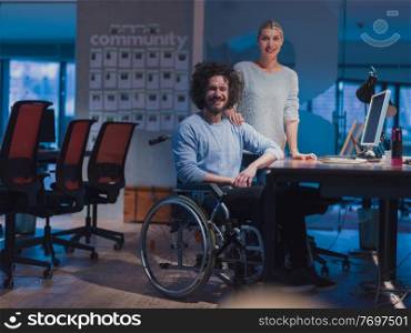 Businessman in a wheelchair in modern coworking office space working late at night in the office. Colleagues in the background. Disability and handicap concept. Selective focus. Businessman in a wheelchair in modern coworking office space working late night in office. Colleagues in background. Disability and handicap concept.