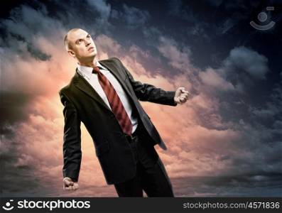 Businessman in anger. Image of young businessman in anger standing against cloudy background